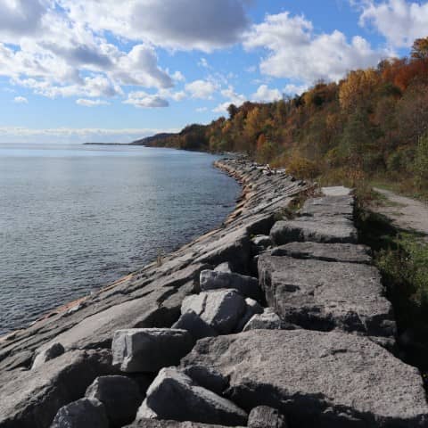 A rocky shoreline beside a large body of water under a partly cloudy sky.